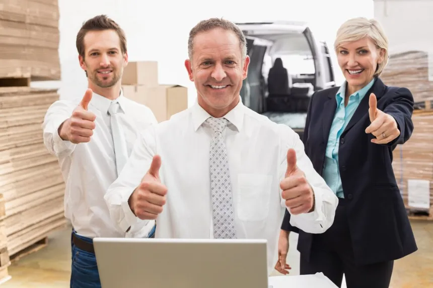 Smiling team gives thumbs up near laptop and boxes; list your business on our business directory to gain sales quickly today